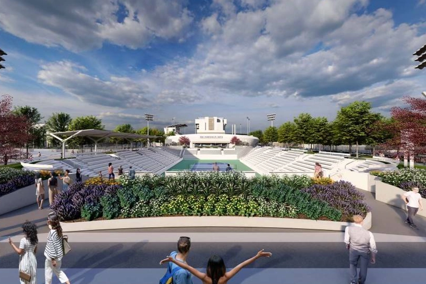 An outdoor amphitheater surrounded by trees and flowerbeds under a partly cloudy blue sky.