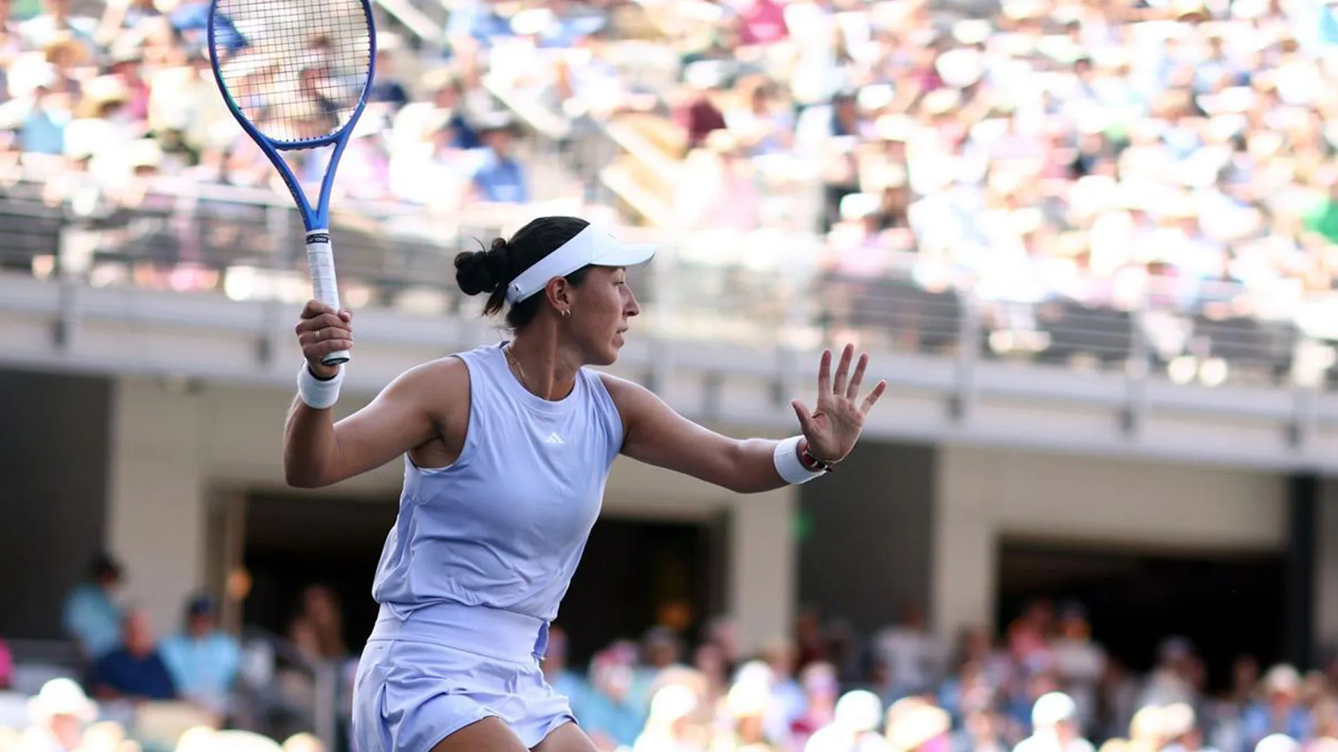 Tennis player in a white outfit preparing to hit a ball with a blue racket, surrounded by spectators.